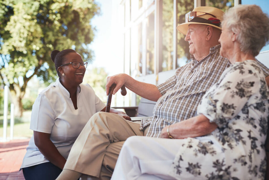 Civitas Senior Living | Senior couple sitting on a bench outside talking and laughing with their caregiver