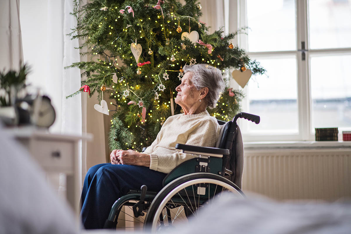 Cambridge Court | A lonely senior woman in wheelchair at home at Christmas time, looking out of a window.