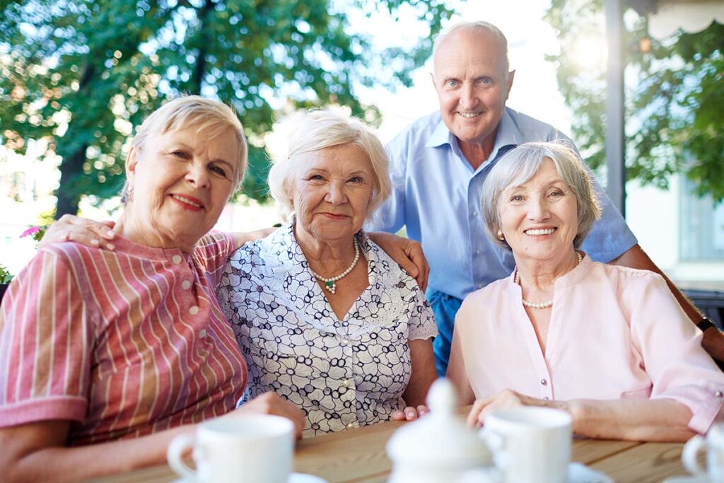 The Avenues of Fort Bend | Our Passionate Leader | Four smiling seniors sitting and standing at a table with coffee