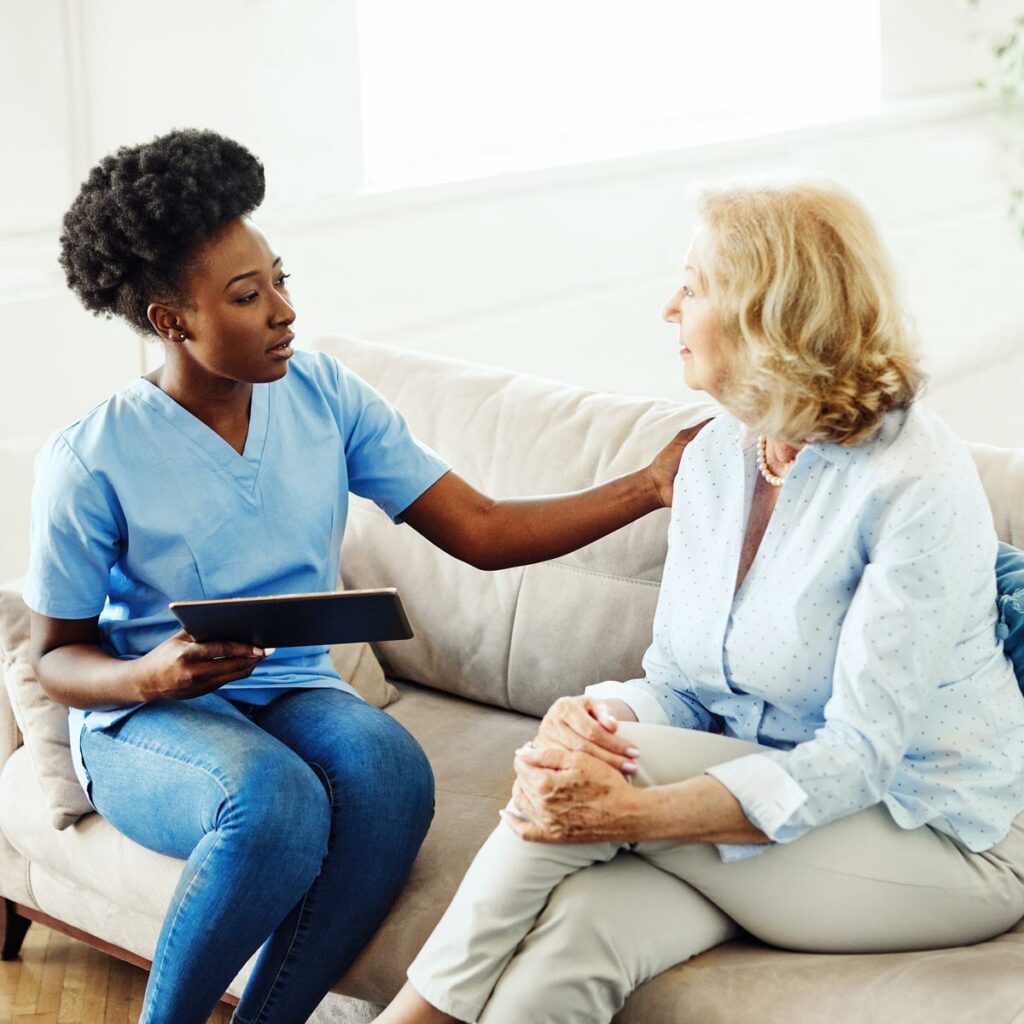 Civitas Senior Living | Senior woman with dementia sitting with associate holding tablet on couch