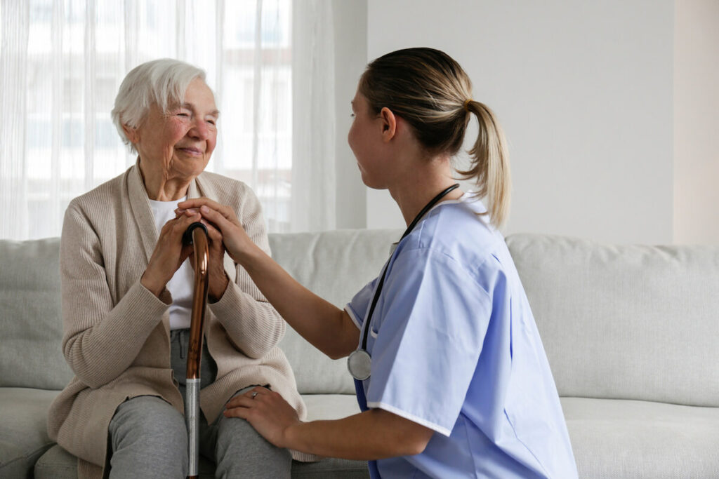Civitas Senior Living | Senior woman with a cain sitting on a couch talking with her caregiver and smiling