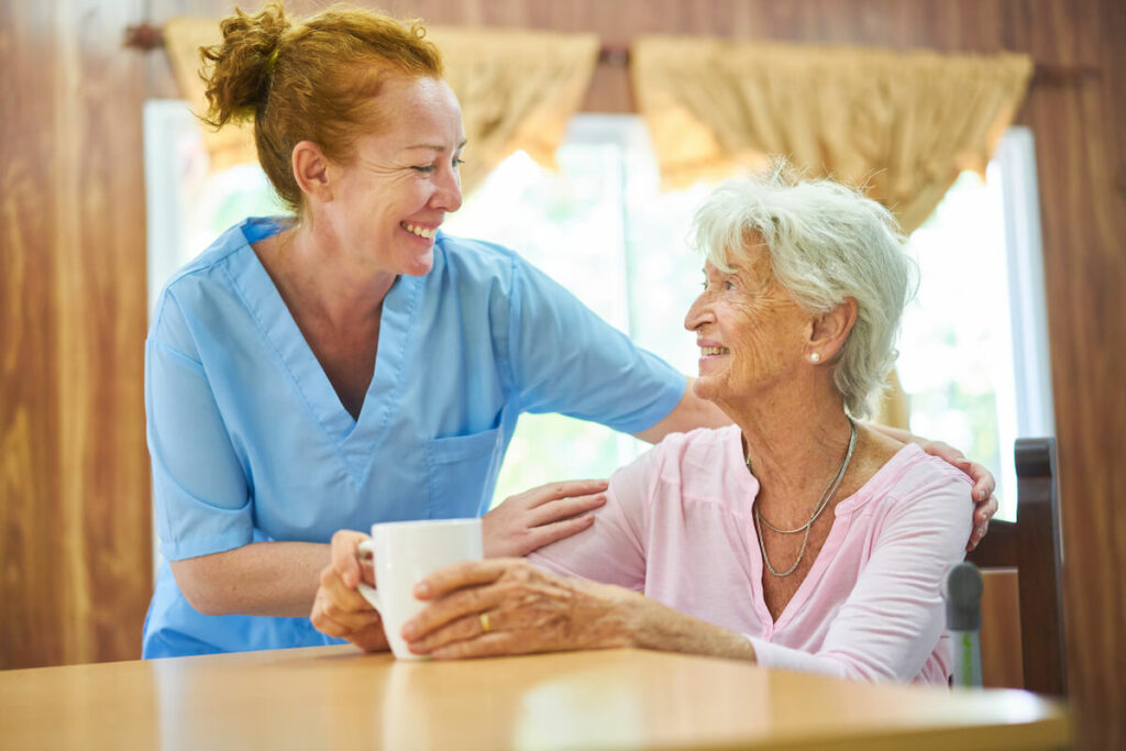 Double Creek | Senior woman smiling at her caregiver while drinking a cup of coffee