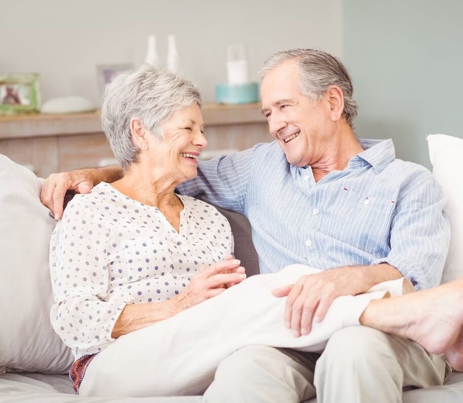 Ledgestone Senior Living | Happy senior couple smiling at eachother while sitting on a couch with their legs across one another