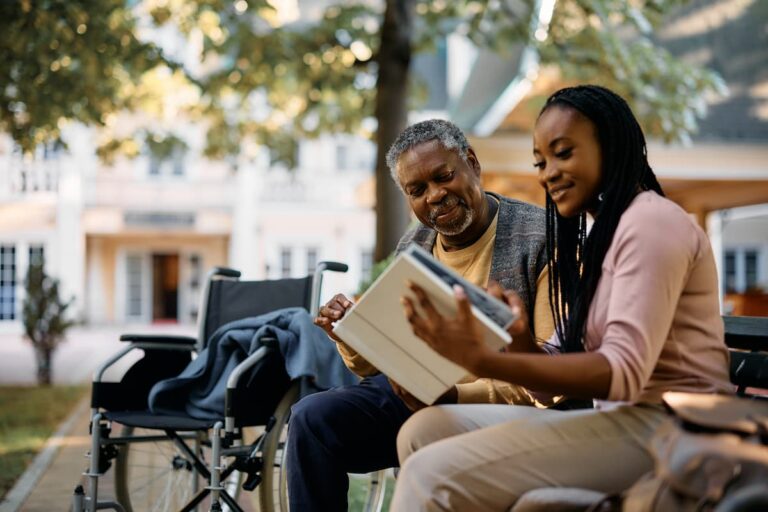 Midtowne | Senior man with caregiver sitting outside on a bench reading a book