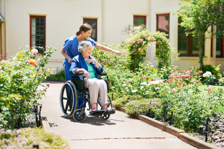 StoneCreek of Flying Horse | Senior woman going for a walk with her caregiver outside while being pushed around in her wheelchair