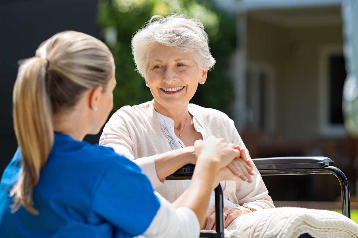 Tech Ridge Oaks | Smiling senior patient sitting on wheelchair with nurse supporting her.