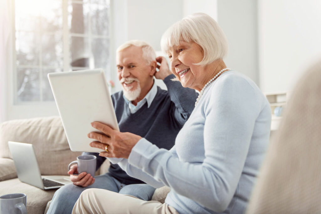 Civitas Senior Living | Senior couple smiling in at a tablet and having coffee on the couch