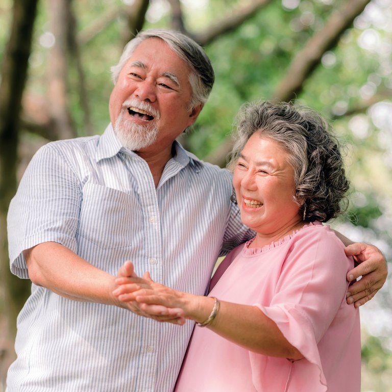 The Grand Senior Living | Senior couple holding hand while laughing under the trees