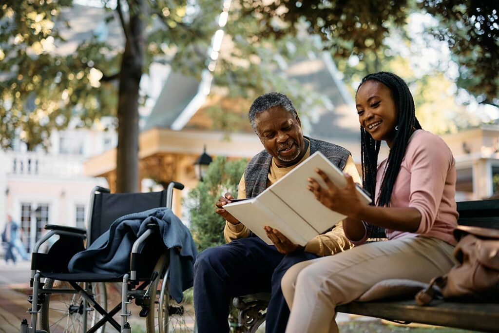 The Grand Senior Living | Senior and caregiver reading a book in the park