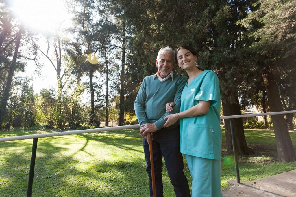 The Grand | Senior man and caregiver walking outside and posing for a picture