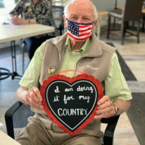 Civitas Senior Living | Senior wearing an American flag mask holding a sign that says "I am doing it for my country""