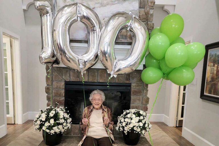 The Hamptons of Tyler | Senior woman holding up balloons that spell out "100"