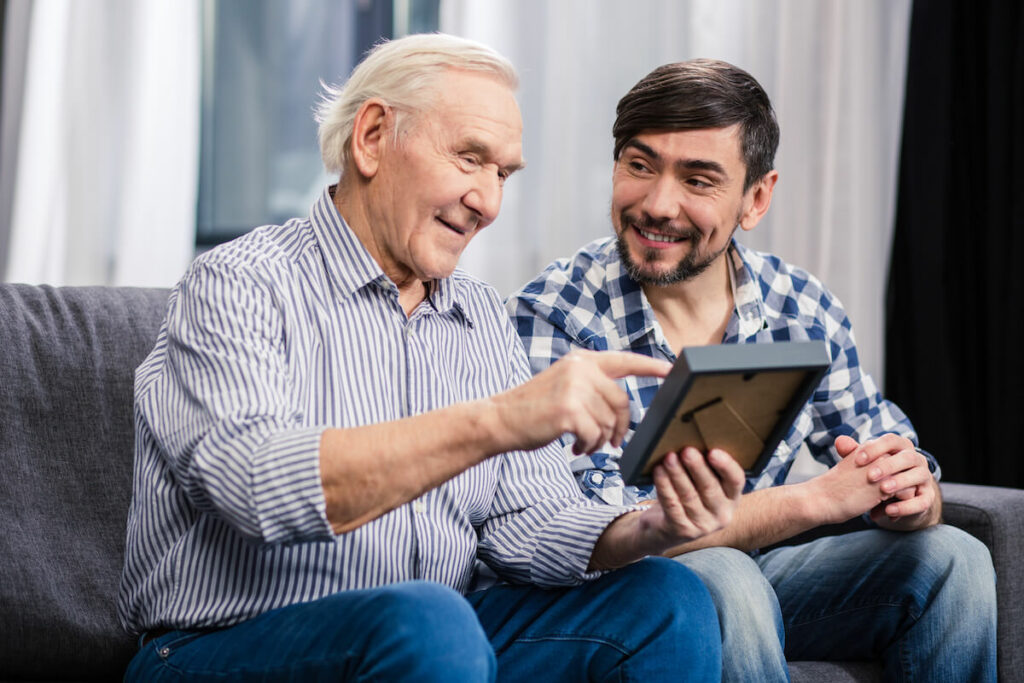 The Grandview of Chisholm Trail | Senior man looking at a photo and pointing while sitting with his caregiver