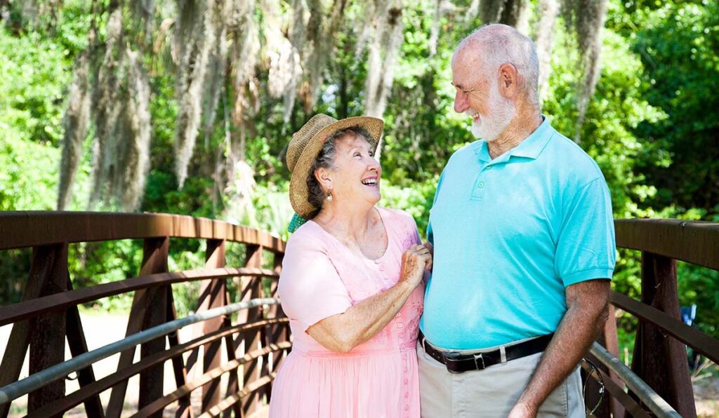 Élan Manatee | Happy retired seniors talking a walk on a bridge under Florida tree moss