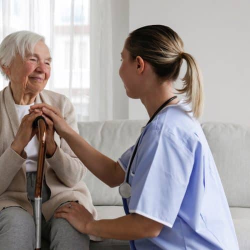 Civitas Senior Living | Senior woman with a cain sitting on a couch talking with her caregiver and smiling