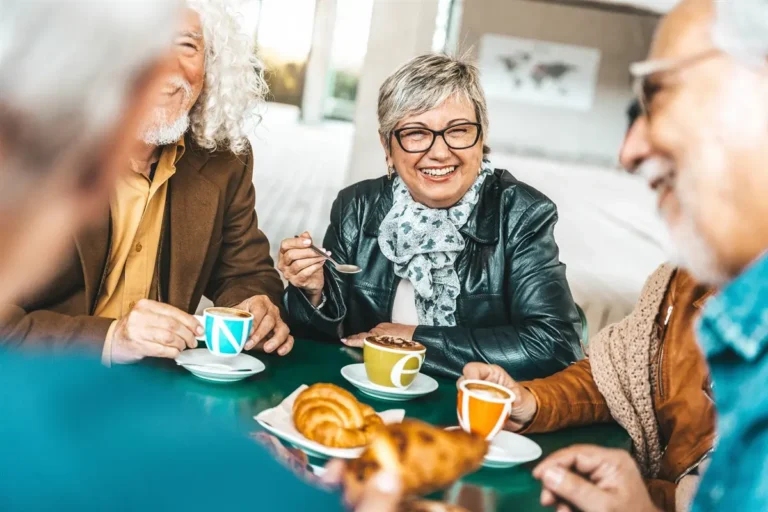 Older adults laughing together over coffee and pastries at a cafe table.