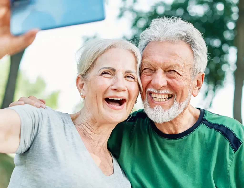 Happy active senior couple having fun using smartphone, taking selfie, or having a video call and wearing sportswear, after having an exercise sport activity outdoors